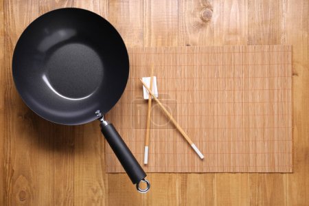 Photo for Empty iron wok and chopsticks on wooden table, top view. Space for text - Royalty Free Image