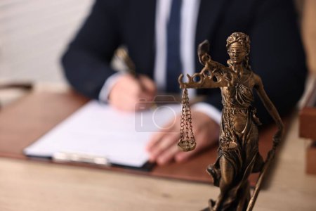 Photo for Notary writing notes at wooden table in office, focus on statue of Lady Justice - Royalty Free Image