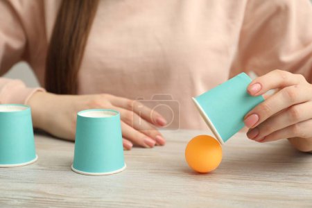 Shell game. Woman showing ball under cup at wooden table, closeup