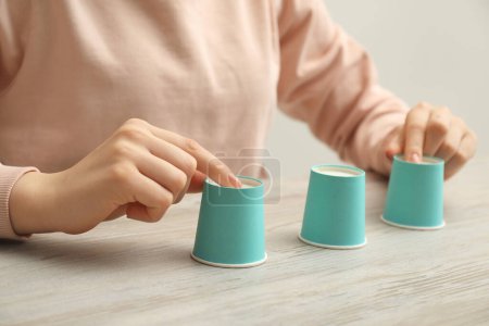 Woman playing shell game with turquoise cups at wooden table, closeup