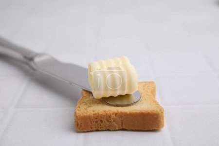 Tasty butter curl, knife and piece of dry bread on white tiled table, closeup