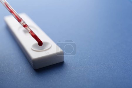 Dropping blood sample onto disposable express test cassette with pipette on blue background, closeup. Space for text