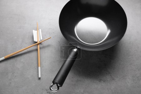 Photo for Empty iron wok and wooden chopsticks on grey table - Royalty Free Image