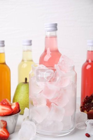 Leckere Kombucha in Flaschen, Glas mit Eis und frischen Früchten auf weißem Tisch