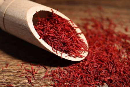 Aromatic saffron and scoop on wooden table, closeup
