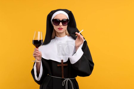 Frau im Ordensgewand hält Glas Wein und Zigarette vor orangefarbenem Hintergrund