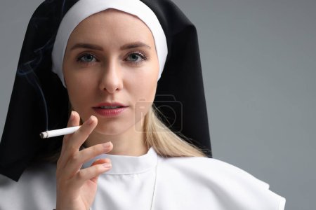 Mujer con hábito de monja fumando cigarrillo sobre fondo gris. Espacio para texto
