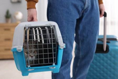 Téléchargez les photos : Voyage avec animal de compagnie. Homme tenant transporteur avec chat mignon et valise à la maison, gros plan - en image libre de droit