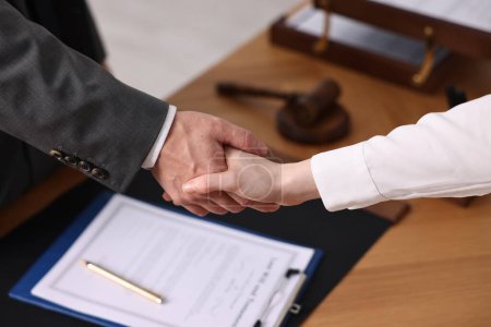 Photo for Notary shaking hands with client at wooden table in office, closeup - Royalty Free Image