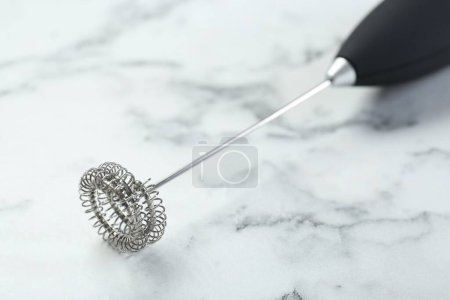Black milk frother wand on white marble table, closeup