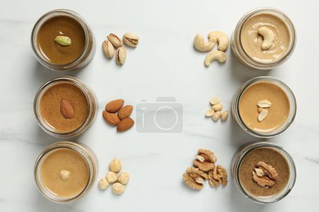Photo for Tasty nut butters in jars and raw nuts on white marble table, flat lay - Royalty Free Image