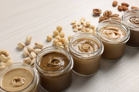 Photo for Many tasty nut butters in jars and nuts on white wooden table, closeup - Royalty Free Image