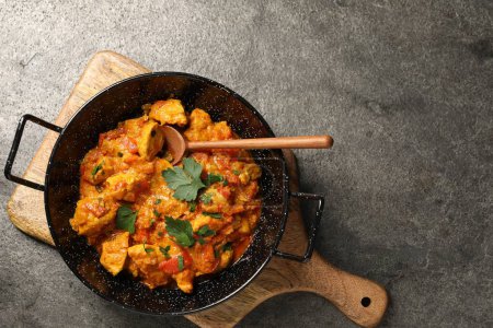 Delicious chicken curry in frying pan and spoon on grey table, top view. Space for text