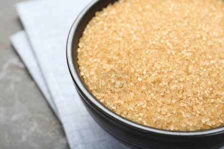 Brown sugar in bowl on grey table, closeup. Space for text