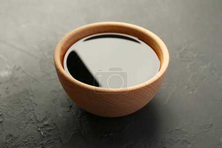 Soy sauce in wooden bowl on black textured table, closeup