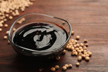 Soy sauce drops falling into bowl on wooden table, closeup. Space for text