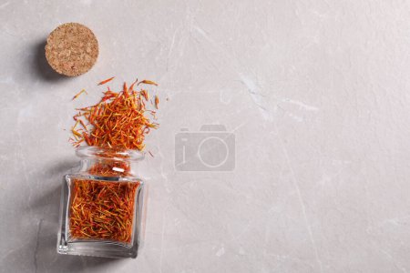 Aromatic saffron and glass jar on light gray table, flat lay. Space for text