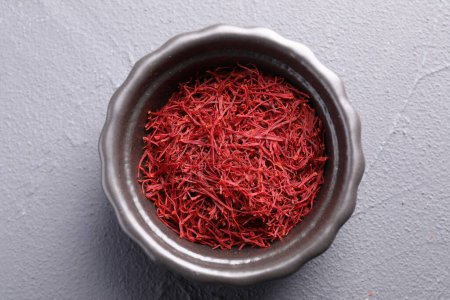 Aromatic saffron in bowl on gray textured table, top view