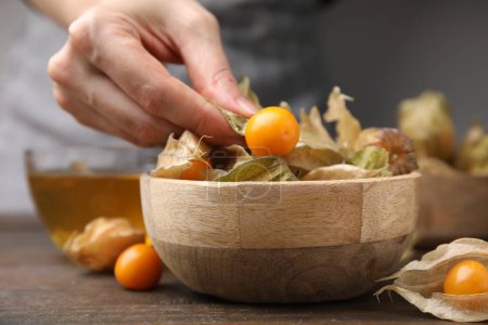 Woman peeling physalis fruit from calyxes at wooden table, closeup