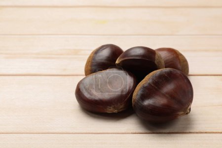 Sweet fresh edible chestnuts on light wooden table, closeup. Space for text