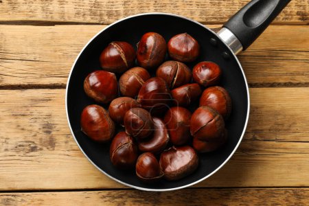 Fresh edible sweet chestnuts in frying pan on wooden table, top view