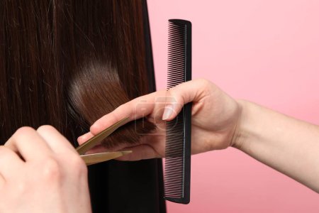 Friseur schneidet Kundin die Haare mit Schere auf rosa Hintergrund, Nahaufnahme