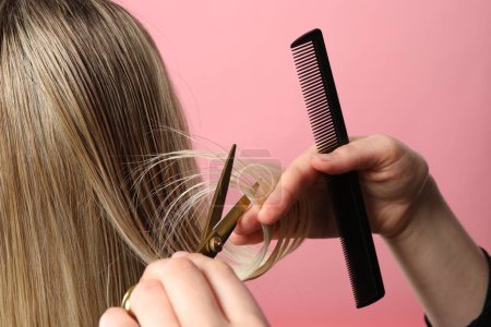 Friseur schneidet Kundin die Haare mit Schere auf rosa Hintergrund, Nahaufnahme