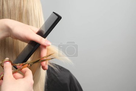 Friseur schneidet Kundin die Haare mit Schere auf hellgrauem Hintergrund, Nahaufnahme. Raum für Text