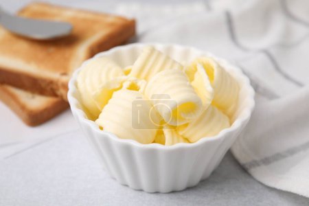 Tasty butter curls in bowl and toasts on light grey table, closeup