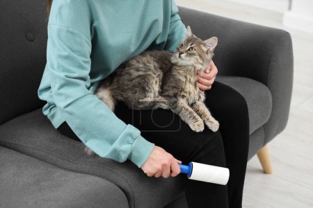 Pet shedding. Woman with lint roller removing cat`s hair from trousers on sofa at home, closeup