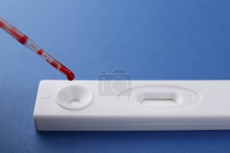 Dropping blood sample onto disposable express test cassette with pipette on blue background, closeup