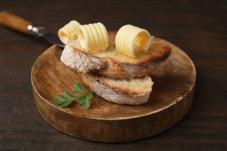 Tasty butter curls and slices of bread on wooden table, closeup