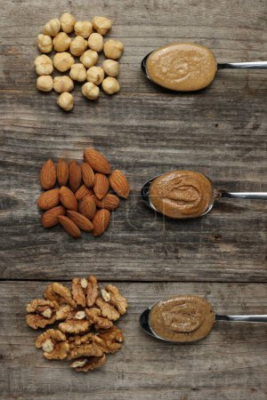 Photo for Tasty nut butters in spoons and raw nuts on wooden table, flat lay - Royalty Free Image
