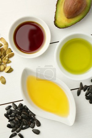 Photo for Vegetable fats. Different cooking oils in bowls and ingredients on white wooden table, flat lay - Royalty Free Image