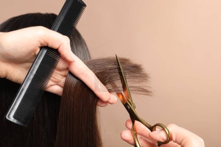 Hairdresser cutting client's hair with scissors on beige background, closeup. Space for text