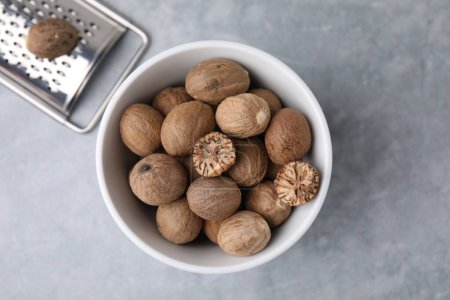 Nutmegs in bowl and metal grater on light grey table, flat lay