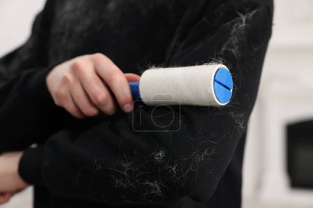Pet shedding. Man with lint roller removing dog's hair from sweater indoors, closeup