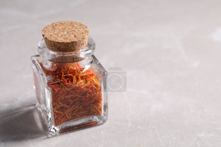 Aromatic saffron and glass jar on light gray table, space for text