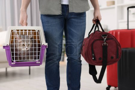 Téléchargez les photos : Voyage avec animal de compagnie. Homme tenant transporteur avec chat mignon et sac à la maison, gros plan - en image libre de droit