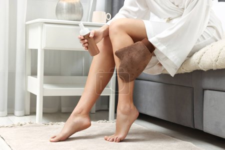 Foto de Auto-bronceado. Mujer que aplica el producto cosmético en la pierna con guante de bronceado en la cama en casa, primer plano - Imagen libre de derechos