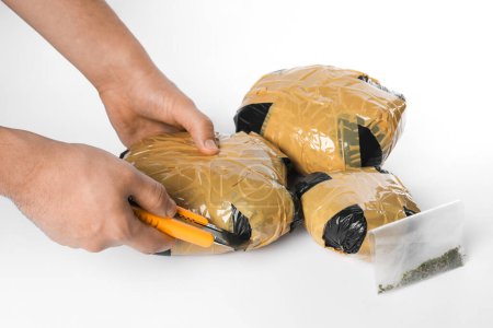 Schmuggel und Drogenhandel. Mann öffnet Packung mit Betäubungsmitteln mit Kastenschneider auf weißem Hintergrund, Nahaufnahme
