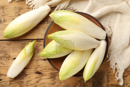 Fresh raw Belgian endives (chicory) and bowl on wooden table, top view