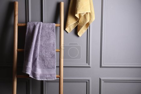 Soft terry towels and wooden ladder indoors, space for text