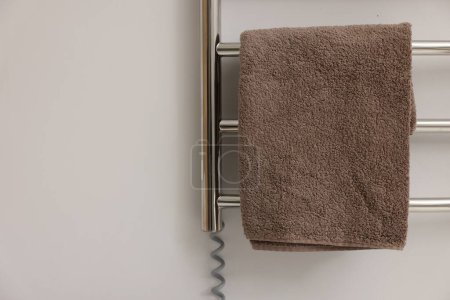 Photo for Heated rail with brown towel on white wall, closeup. Space for text - Royalty Free Image