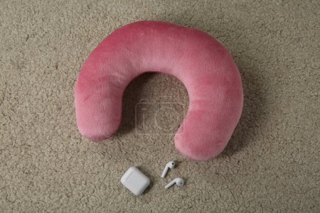 Pink travel pillow and earphones on beige rug, flat lay