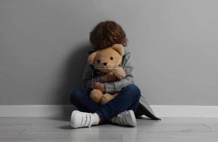 Kindesmissbrauch. Verärgerter Junge mit Spielzeug sitzt auf dem Boden neben grauer Wand