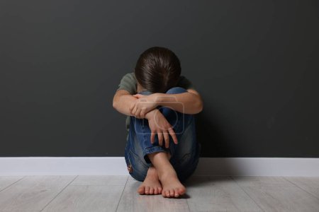 Kindesmissbrauch. Aufgebrachtes Mädchen sitzt auf dem Boden neben grauer Wand