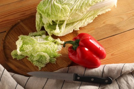 Fresh Chinese cabbage, pepper and knife on wooden table, above view