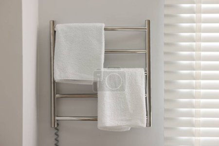 Heated rail with towels on white wall in bathroom