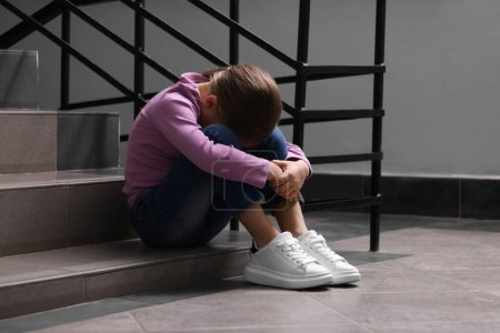 Child abuse. Upset girl sitting on stairs